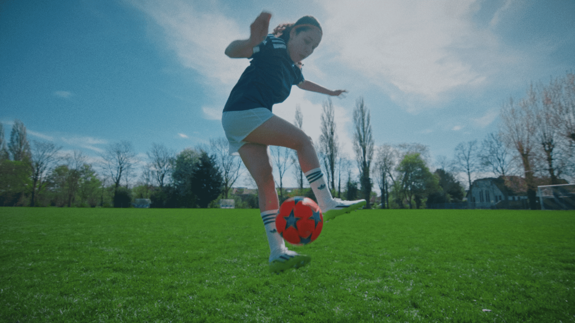 Young girl kicking a soccer ball on a sunny field.