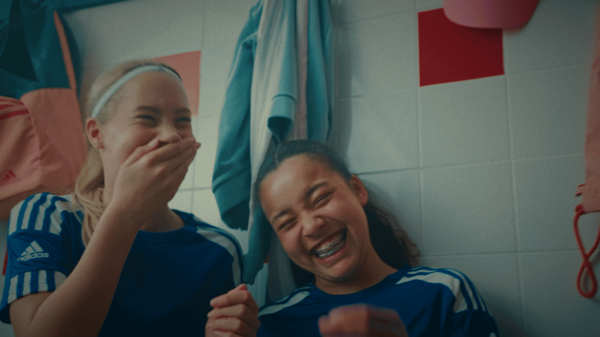 Happy team of women in sports uniforms laughing together in a locker room.