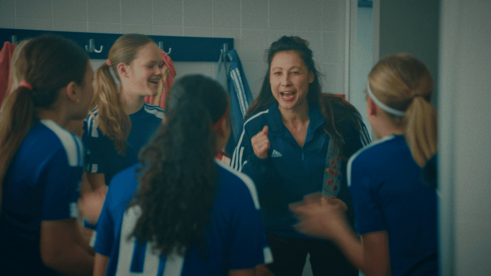 Group of young girls in sports uniforms listening to coach in locker room.