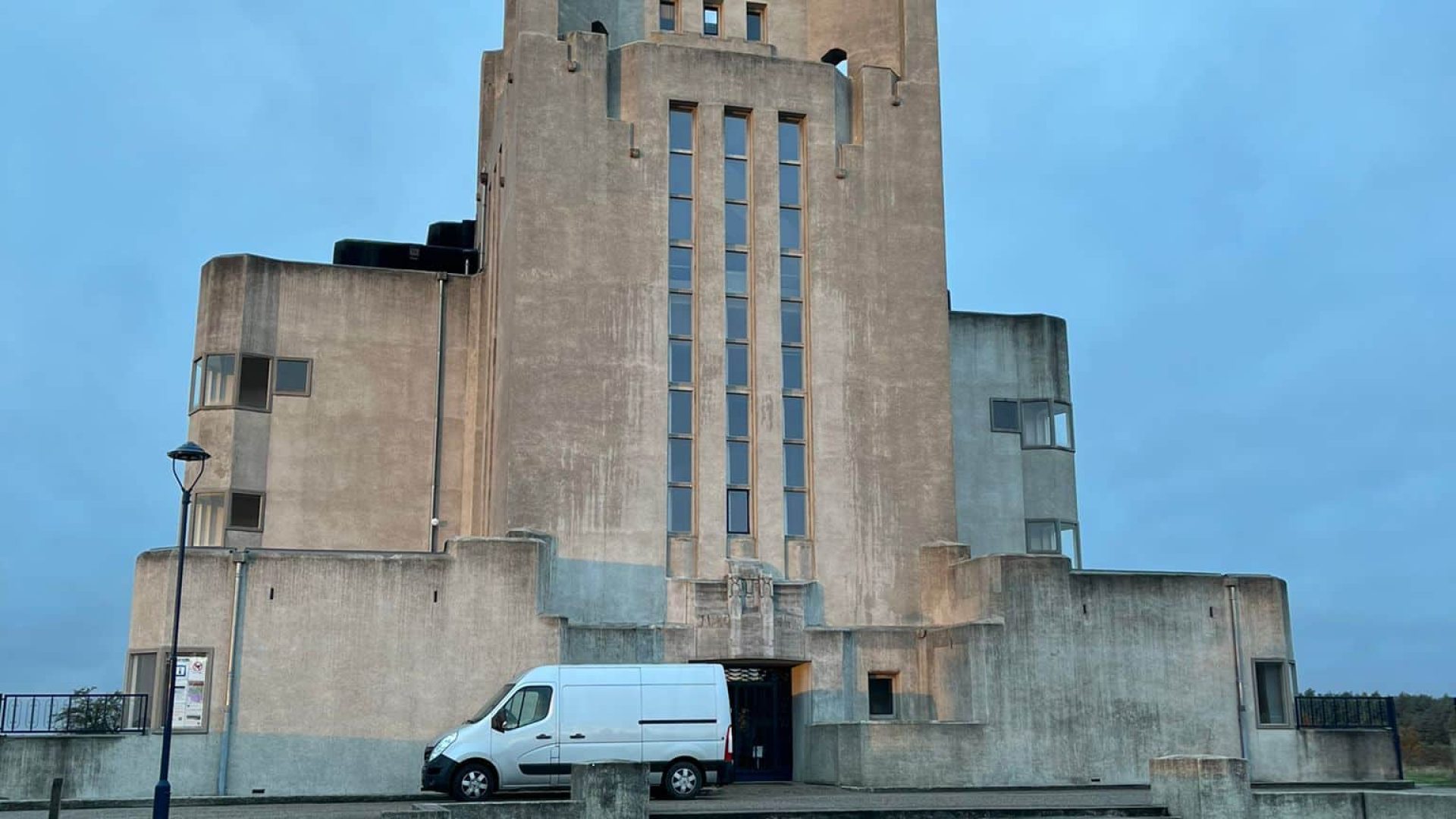 Modern concrete building with water feature in front, under a cloudy sky.