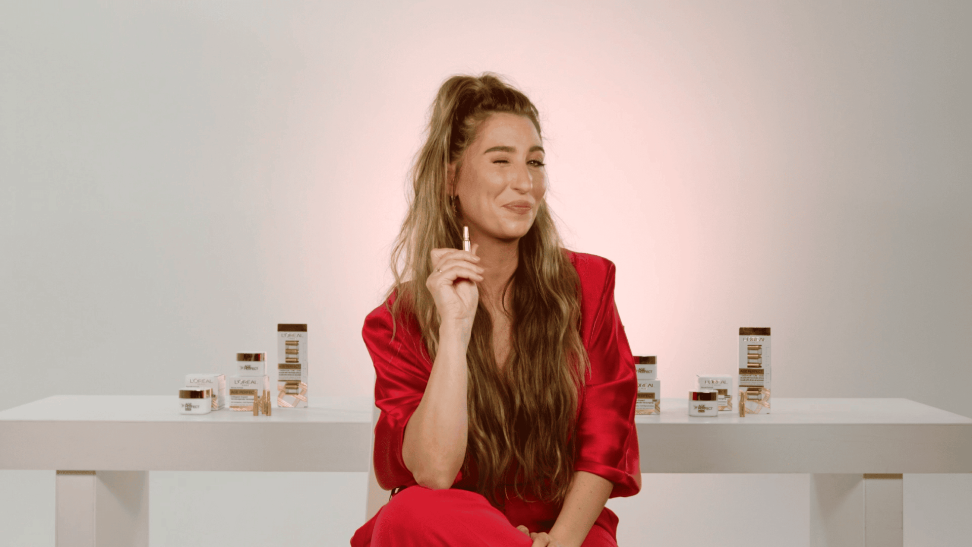 Woman in red blazer with long hair, smiling thoughtfully in a creative workspace.