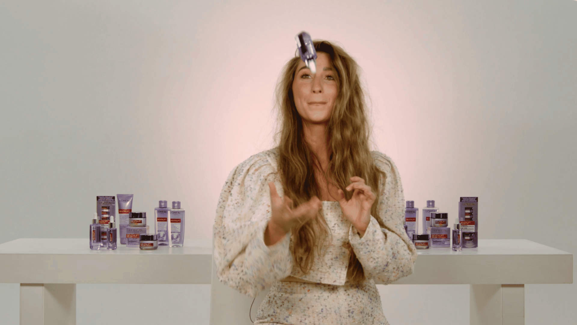 A woman presenting skincare products in a professional setting, emphasizing branding and product sho.