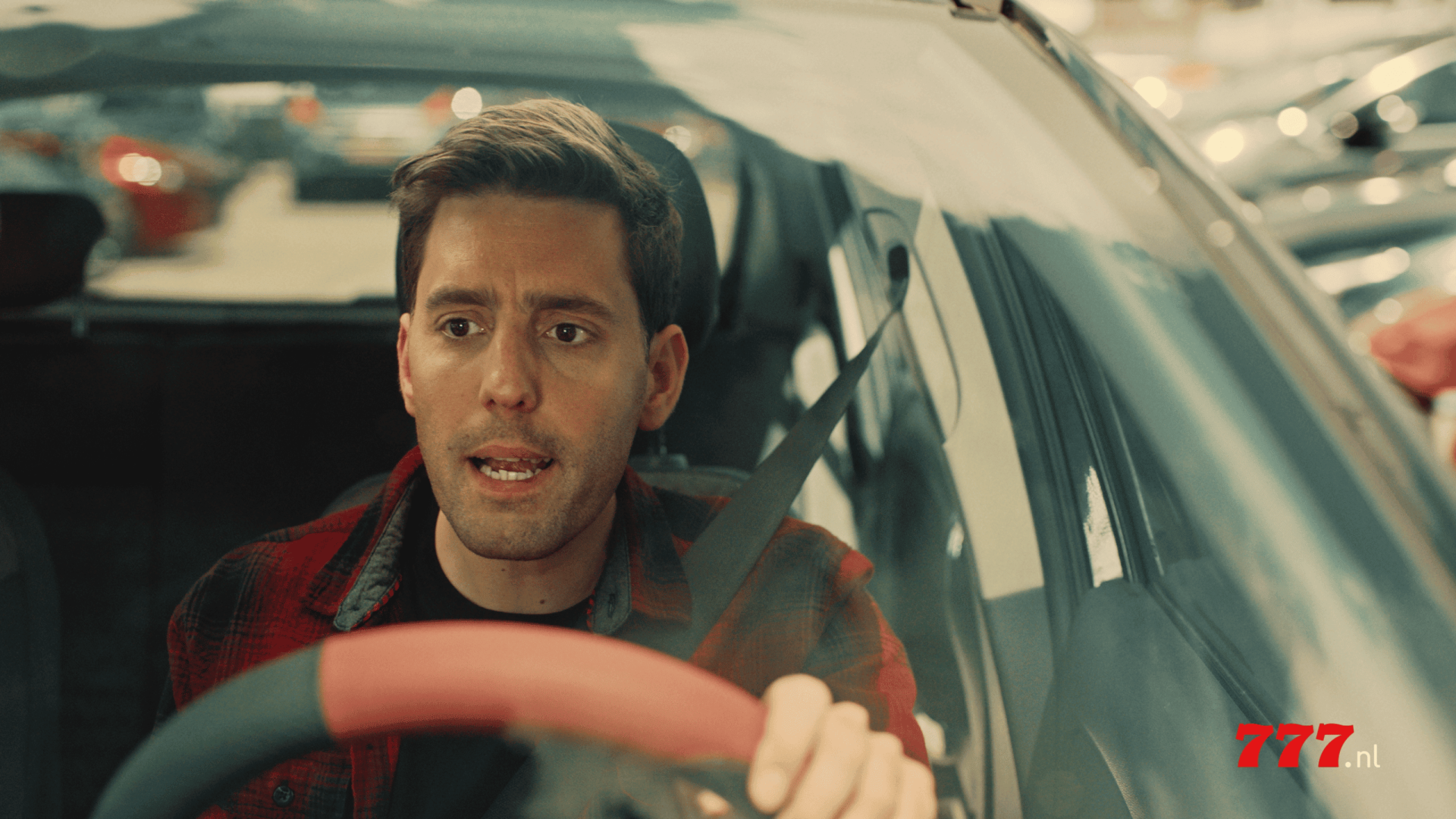 Man driving a car, expressing concern, in a parking lot setting.