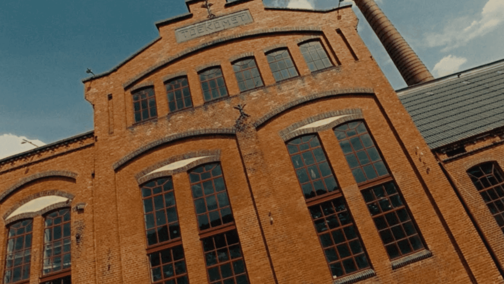 Historic brick factory building with large windows and a chimney.