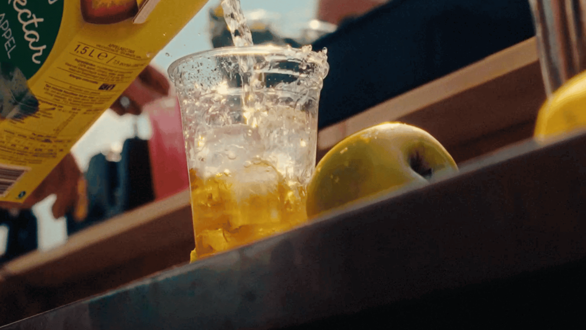 Pouring juice into a glass with fruit on a kitchen counter, bright and vibrant scene.