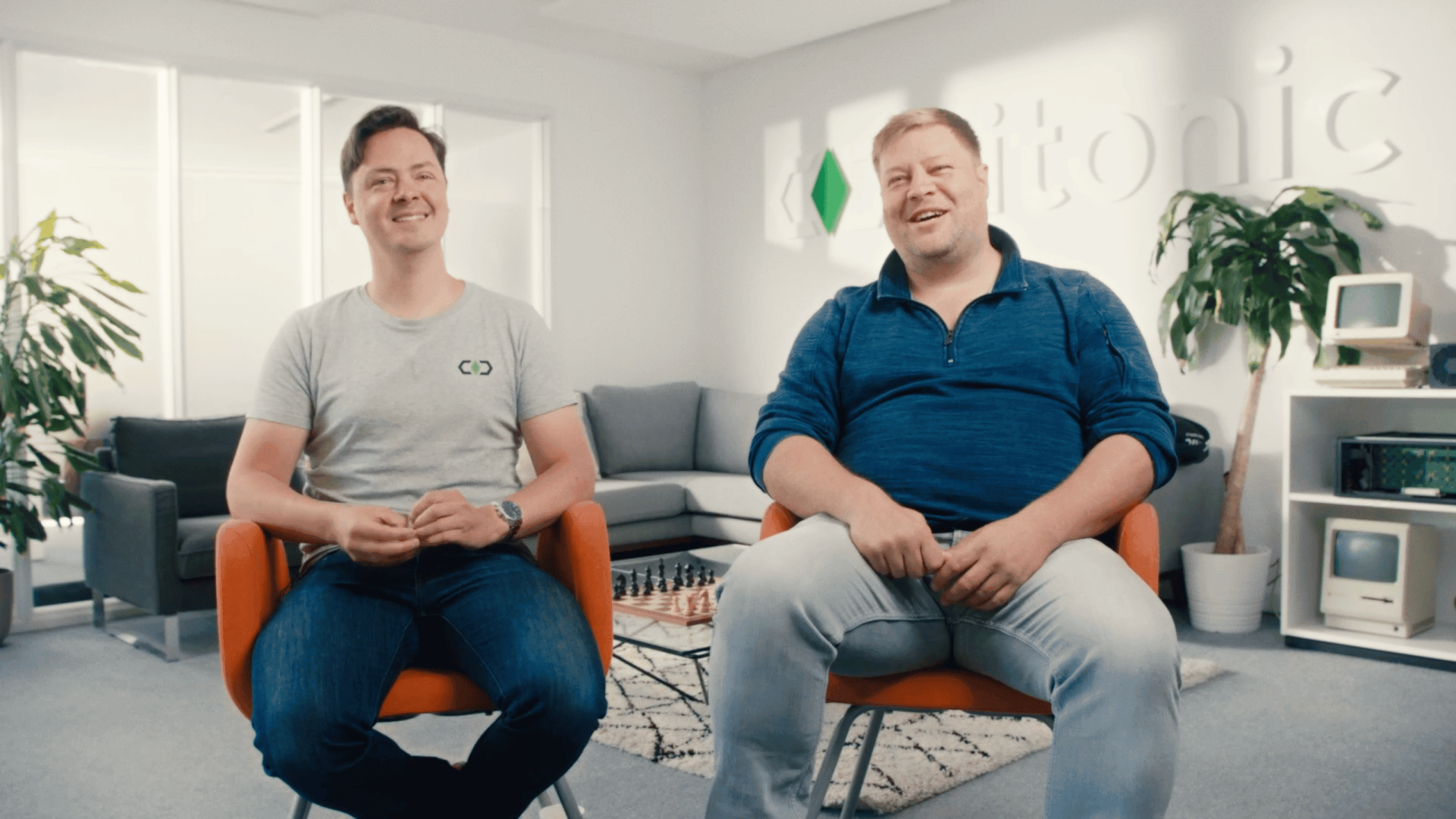 Two smiling men sitting in a modern office, representing Waves Video Agency team.