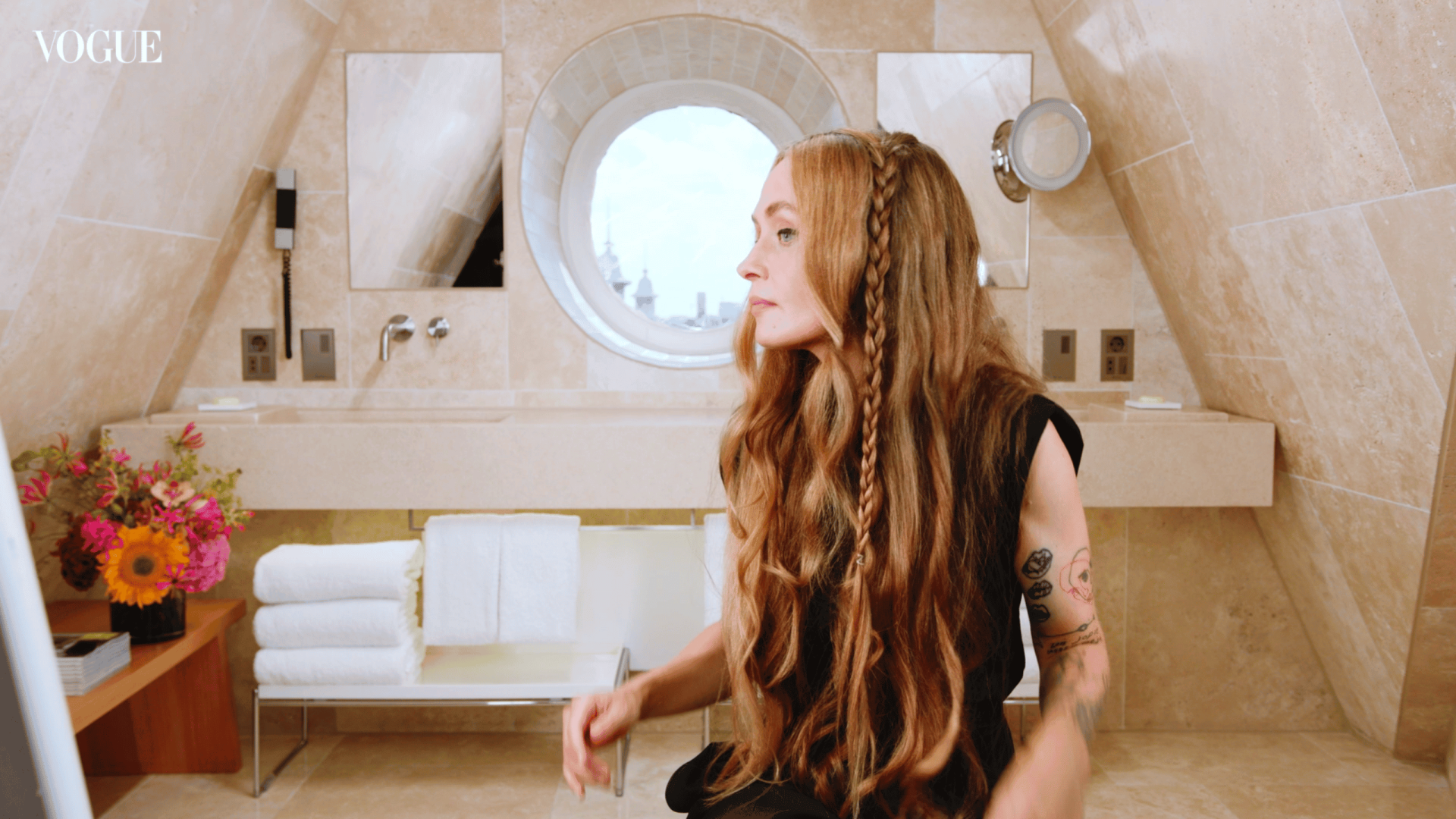 Woman with long red hair in modern bathroom with round window.