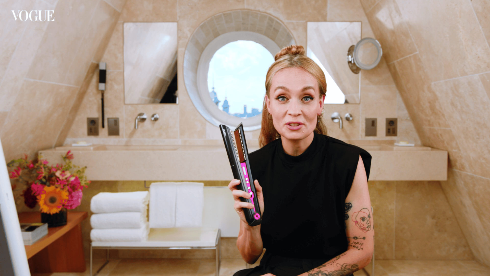 Woman using a flat iron to style her hair in a stylish bathroom setting.