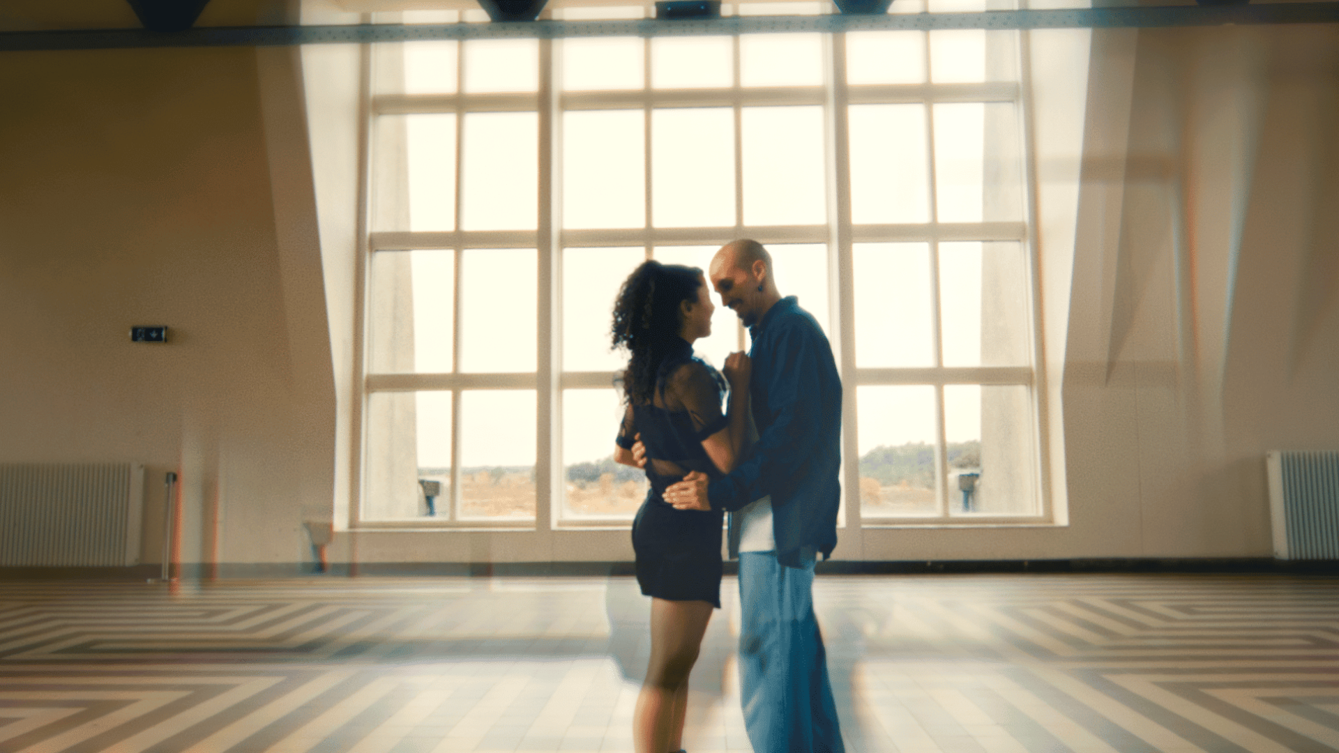 Couple dancing in a spacious studio with large windows, capturing a creative and dynamic atmosphere.