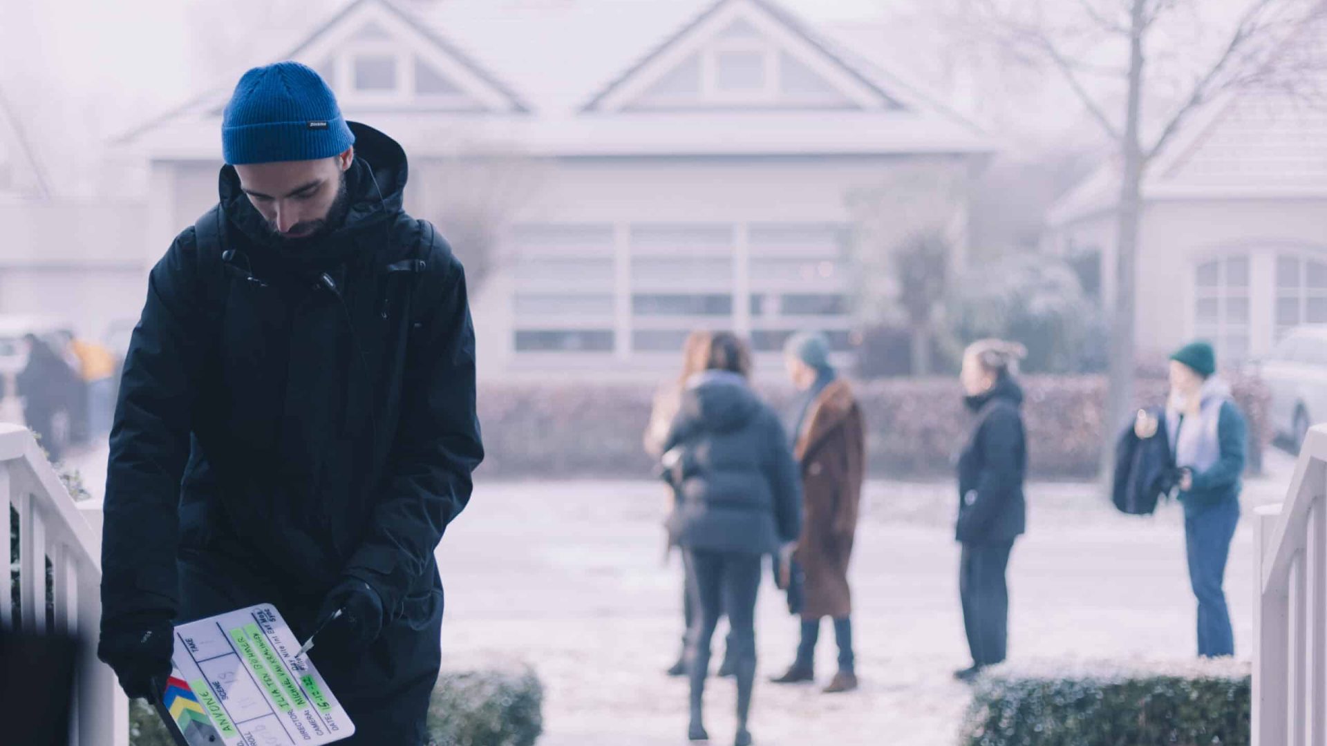 Man holding a clapperboard outdoors in a snowy setting.