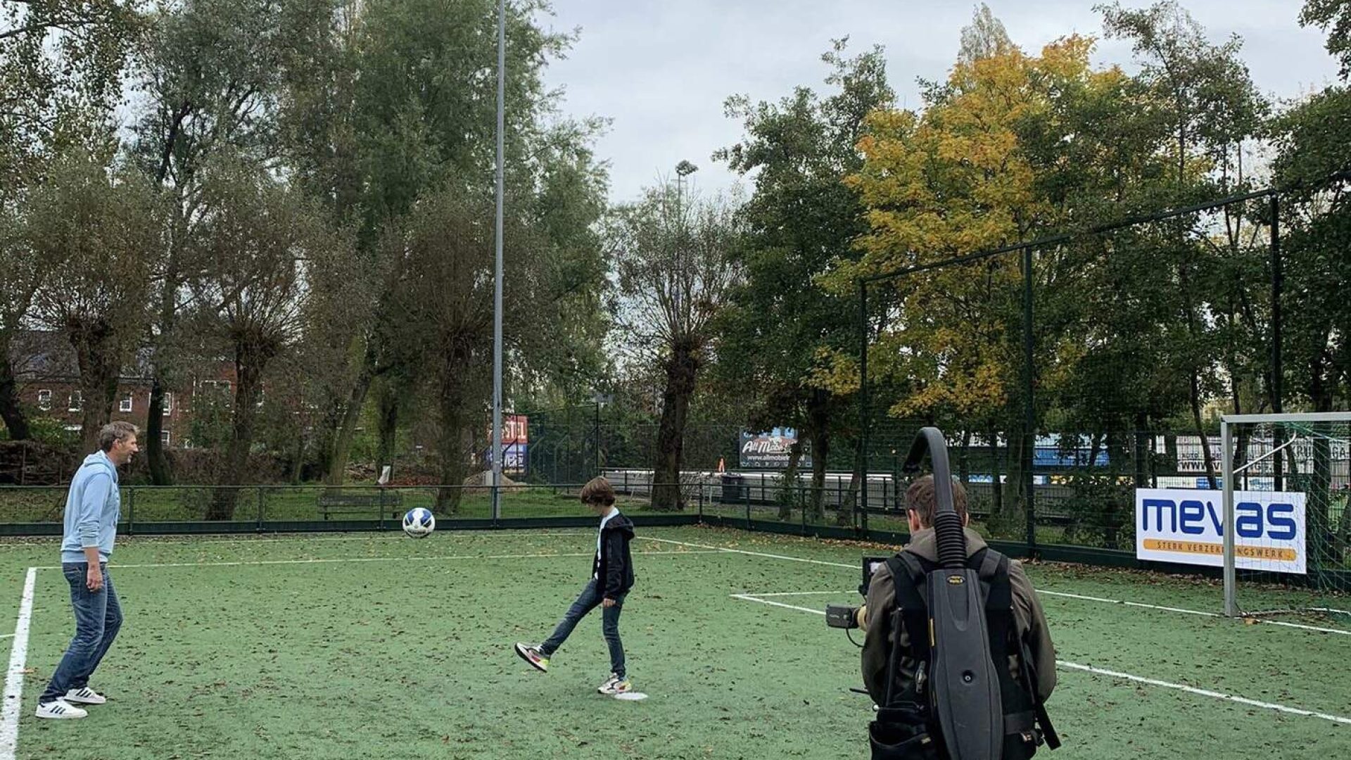 People playing soccer on a field with trees in the background.